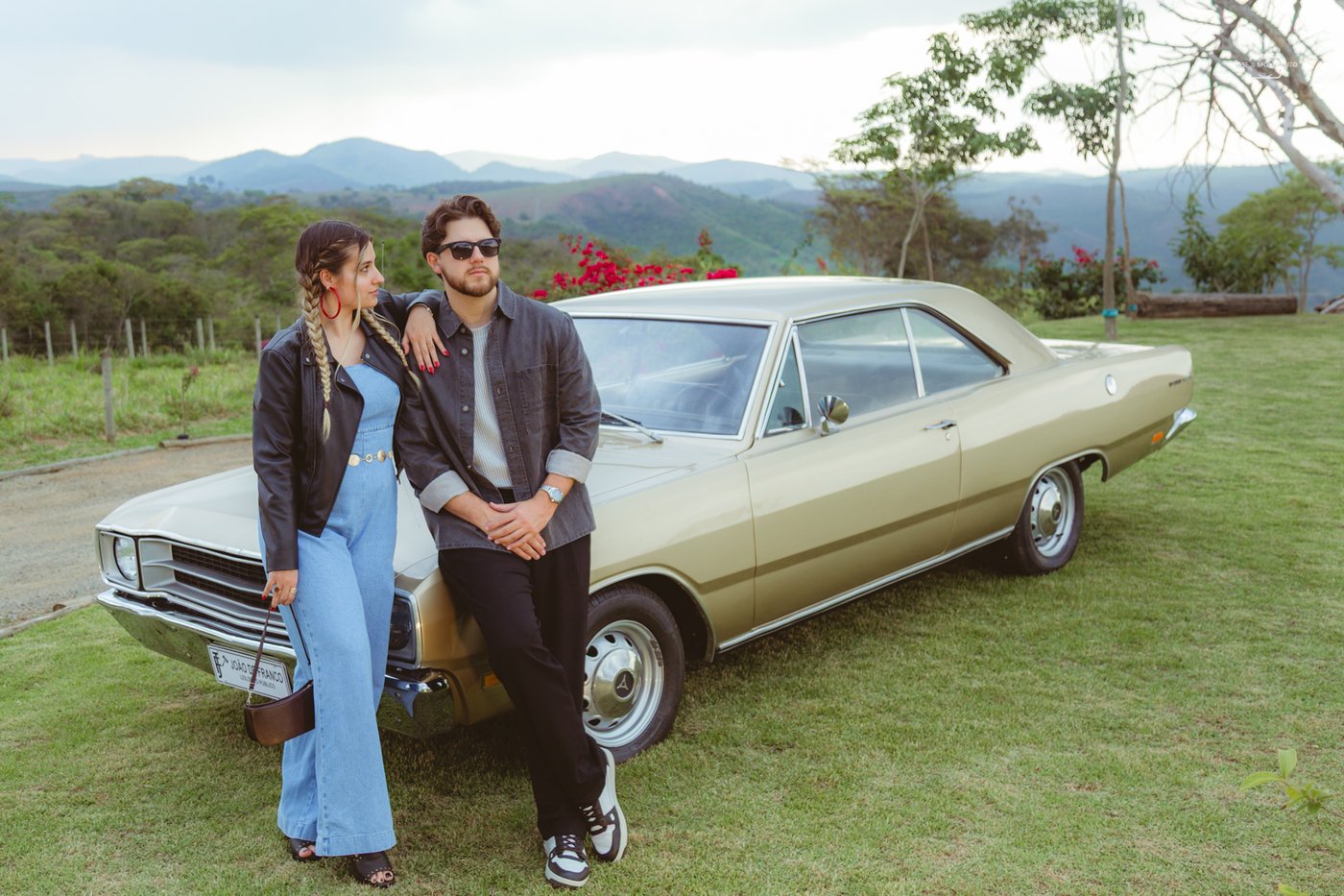 Casal encostado em um Dodge Dart clássico com a serra ao fundo