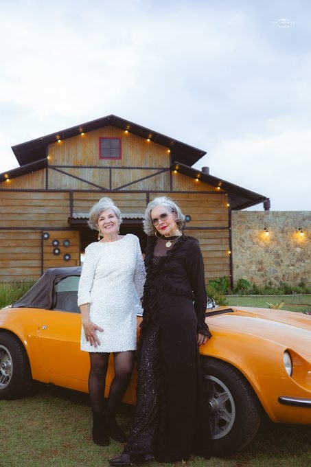 Duas convidadas elegantes ao lado de um carro clássico laranja